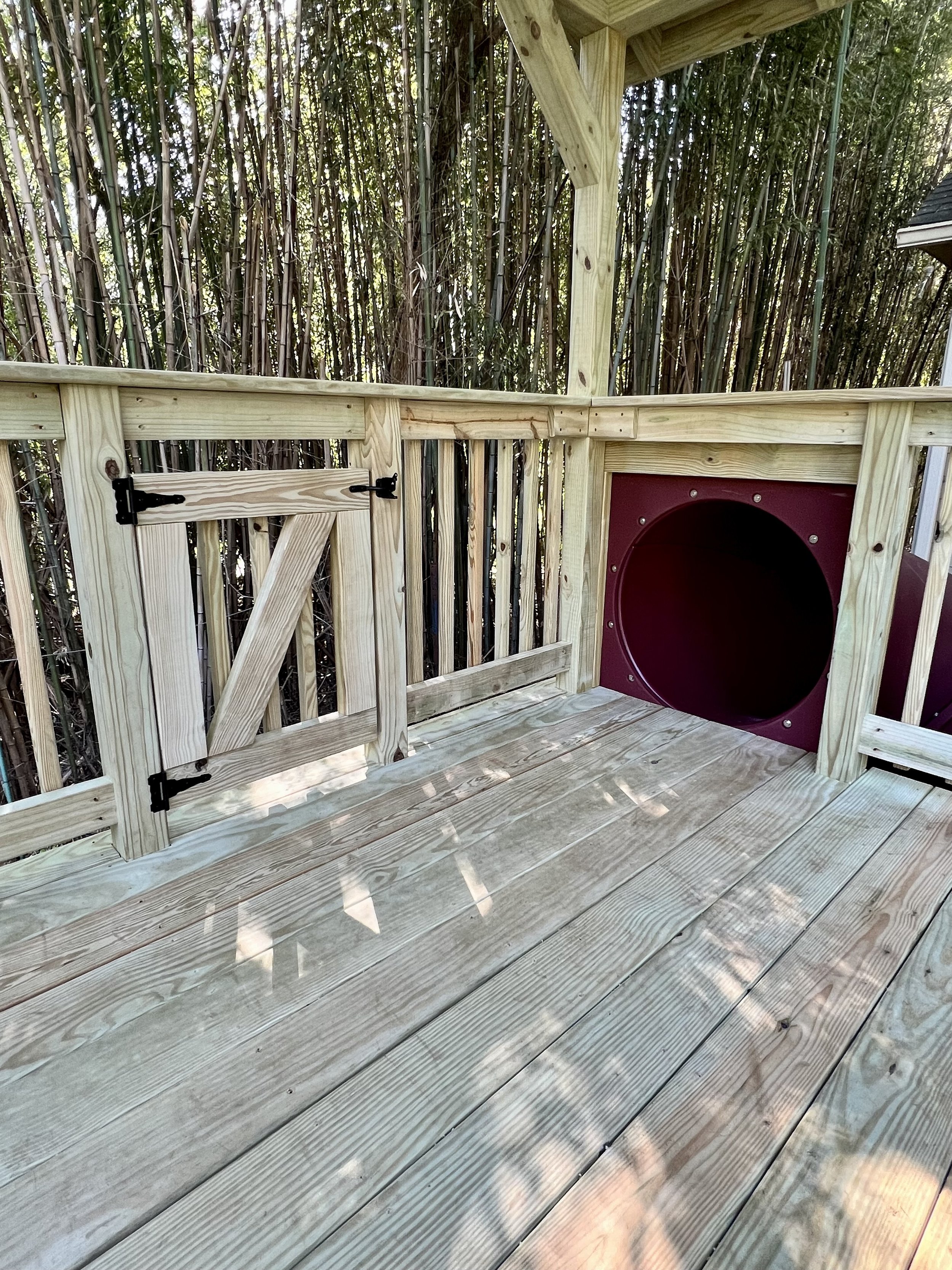 A new wooden outdoor deck with railing, overlooking a fence made of tall bamboo plants.