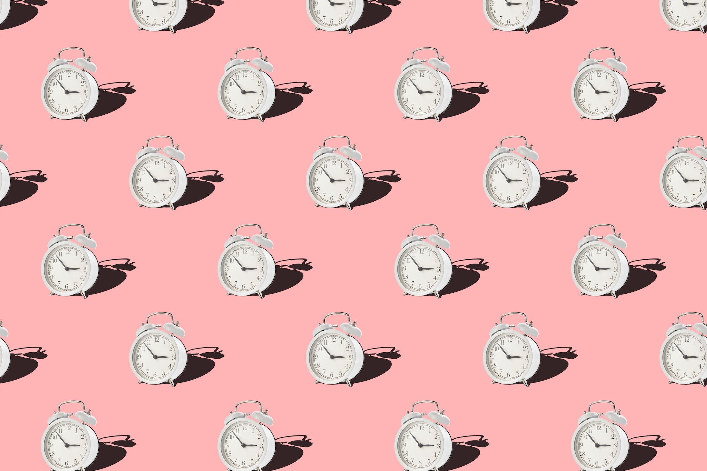 A repetitive pattern of white vintage alarm clocks on a solid pink background, symbolizing time management, daily routines, and consistent habits.