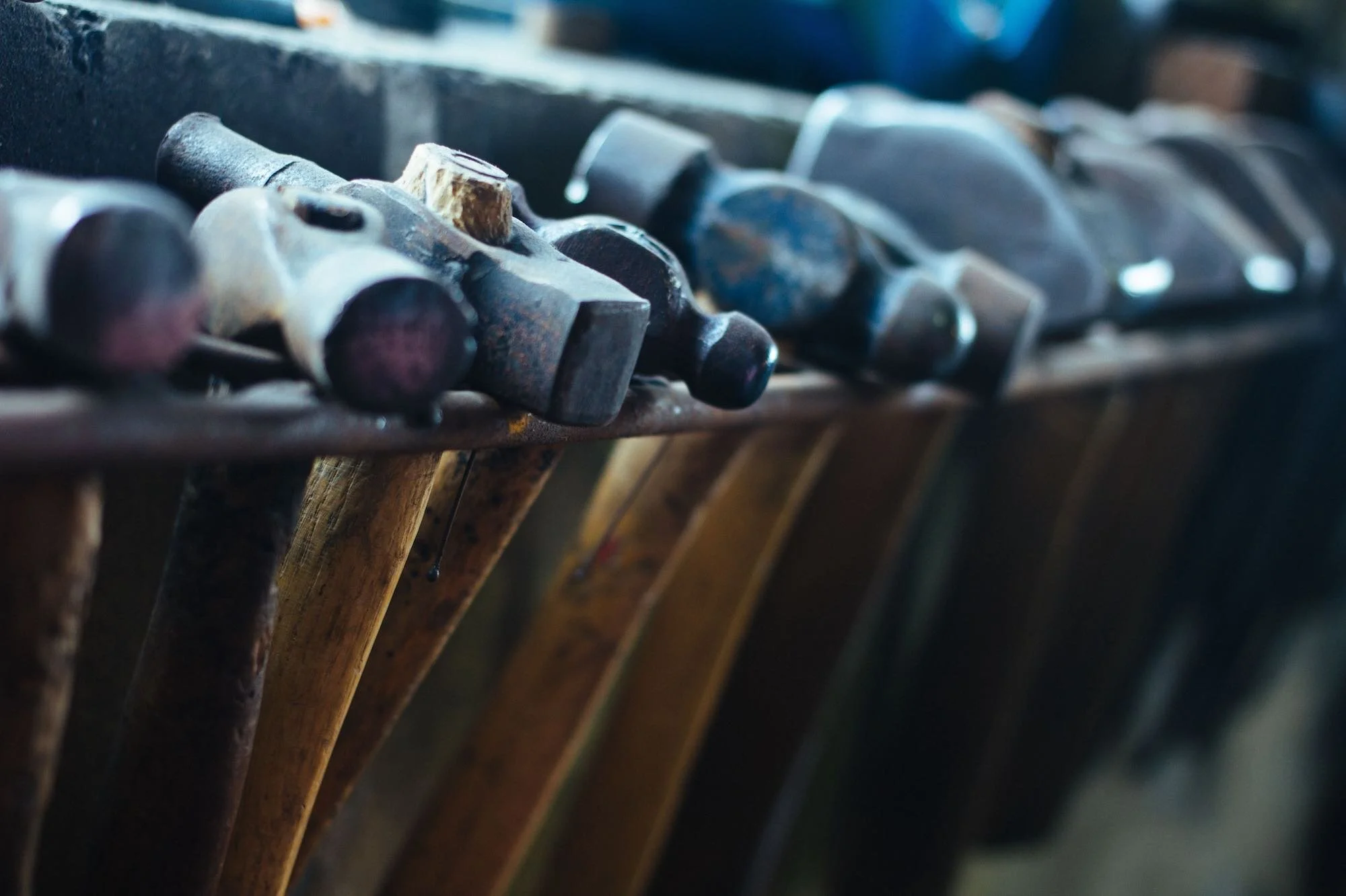A close up view of a row of well used wooden handled hammers resting on a metal shelf rack in a workshop, symbolizing practical retail tools.