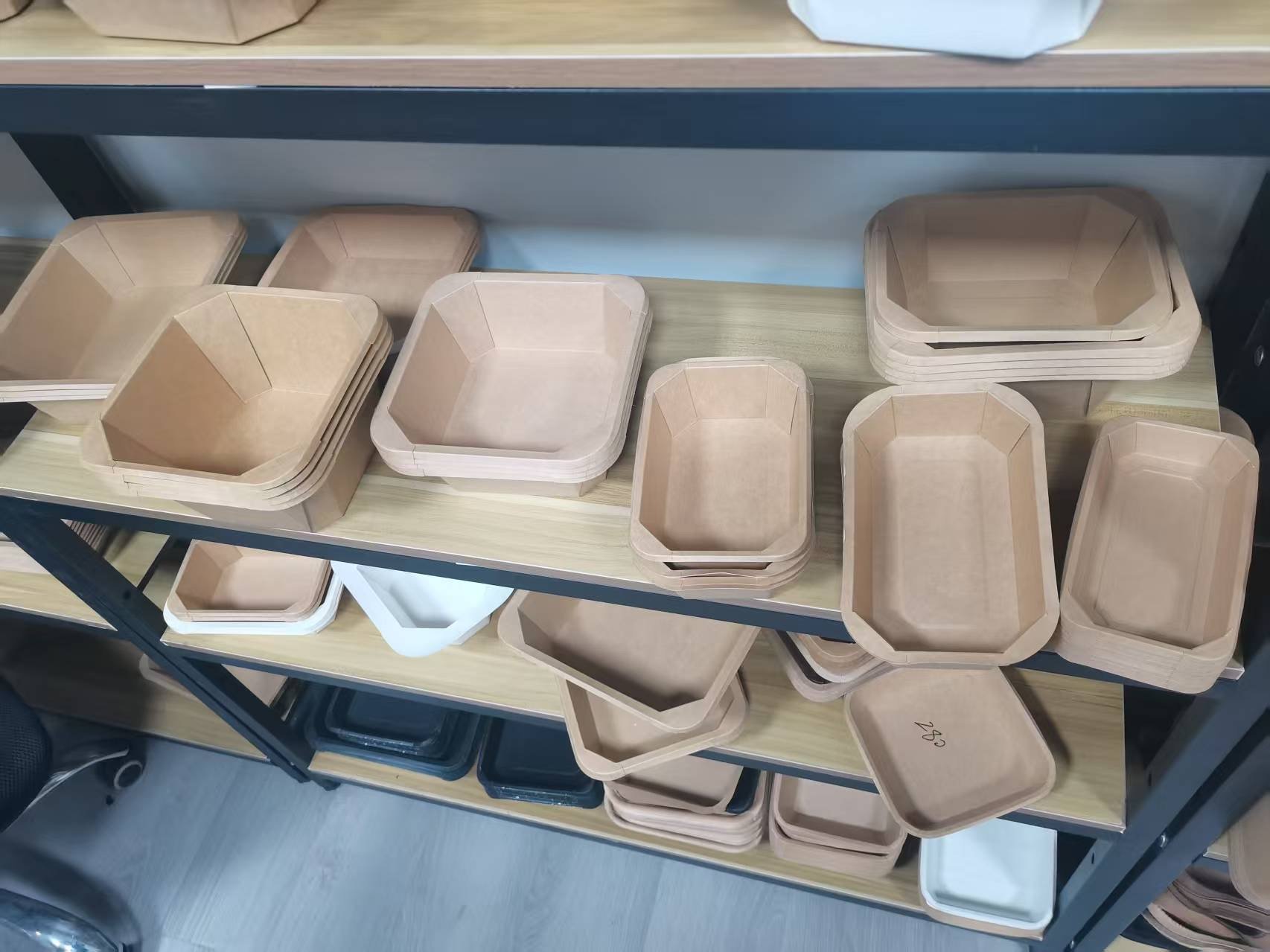 Stacked rectangular and octagonal food containers made of light-colored wood or bamboo on a metal and wood shelving unit.