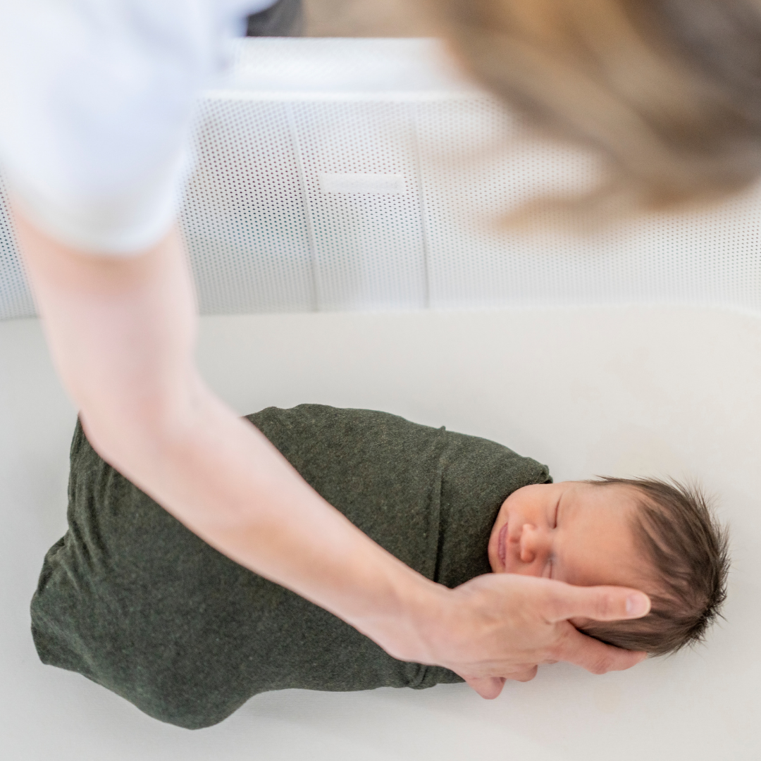 swaddled baby with person touching their head