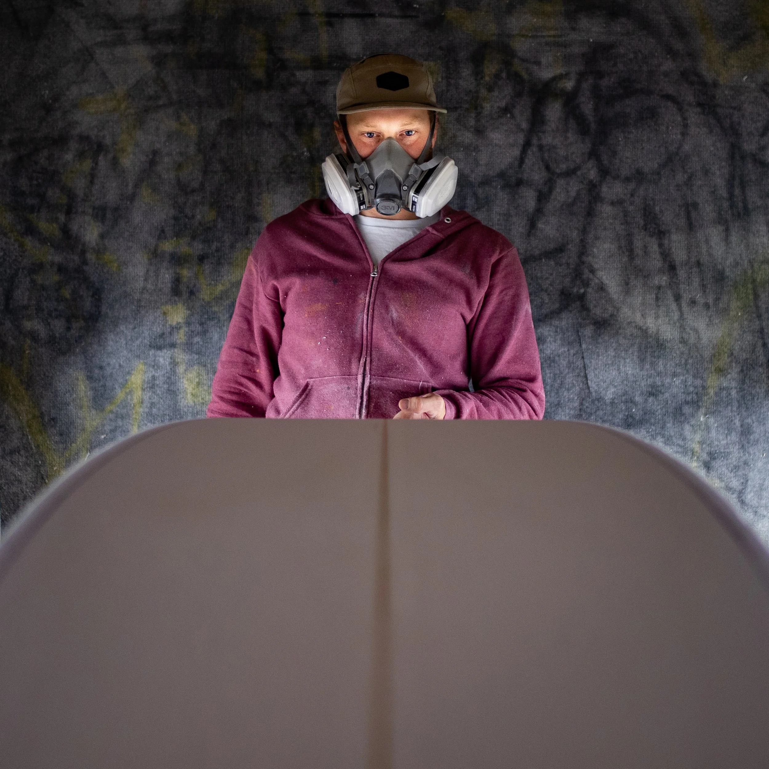 Person wearing a mask shaping a surfboard.