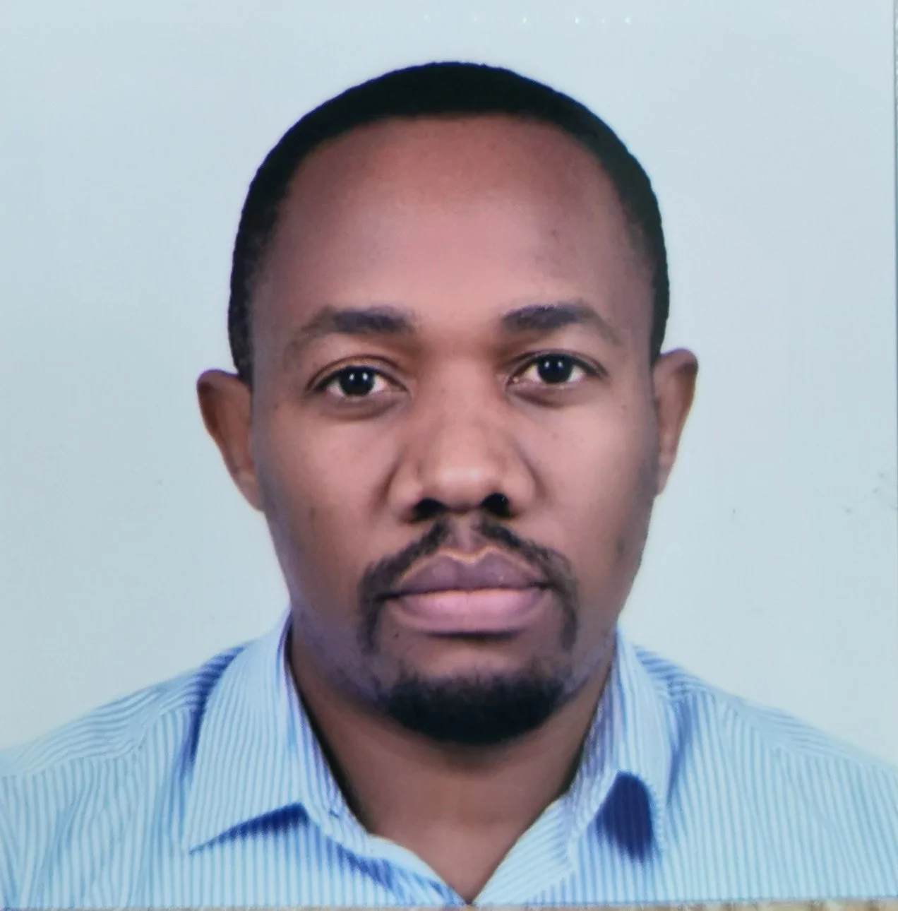 A headshot of a man with short black hair, a goatee, wearing a light blue collared shirt, against a plain white background.