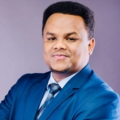 Professional man in a blue suit and tie, with a confident expression, against a gray background.