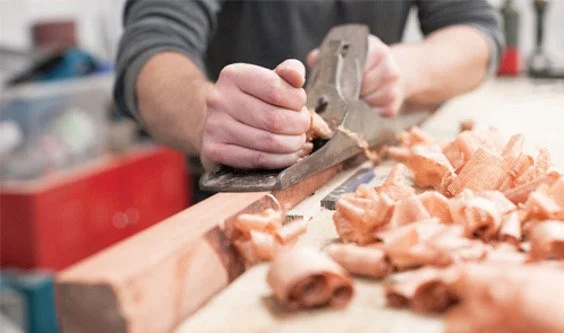 hands planing timber surrounded by wood shavings