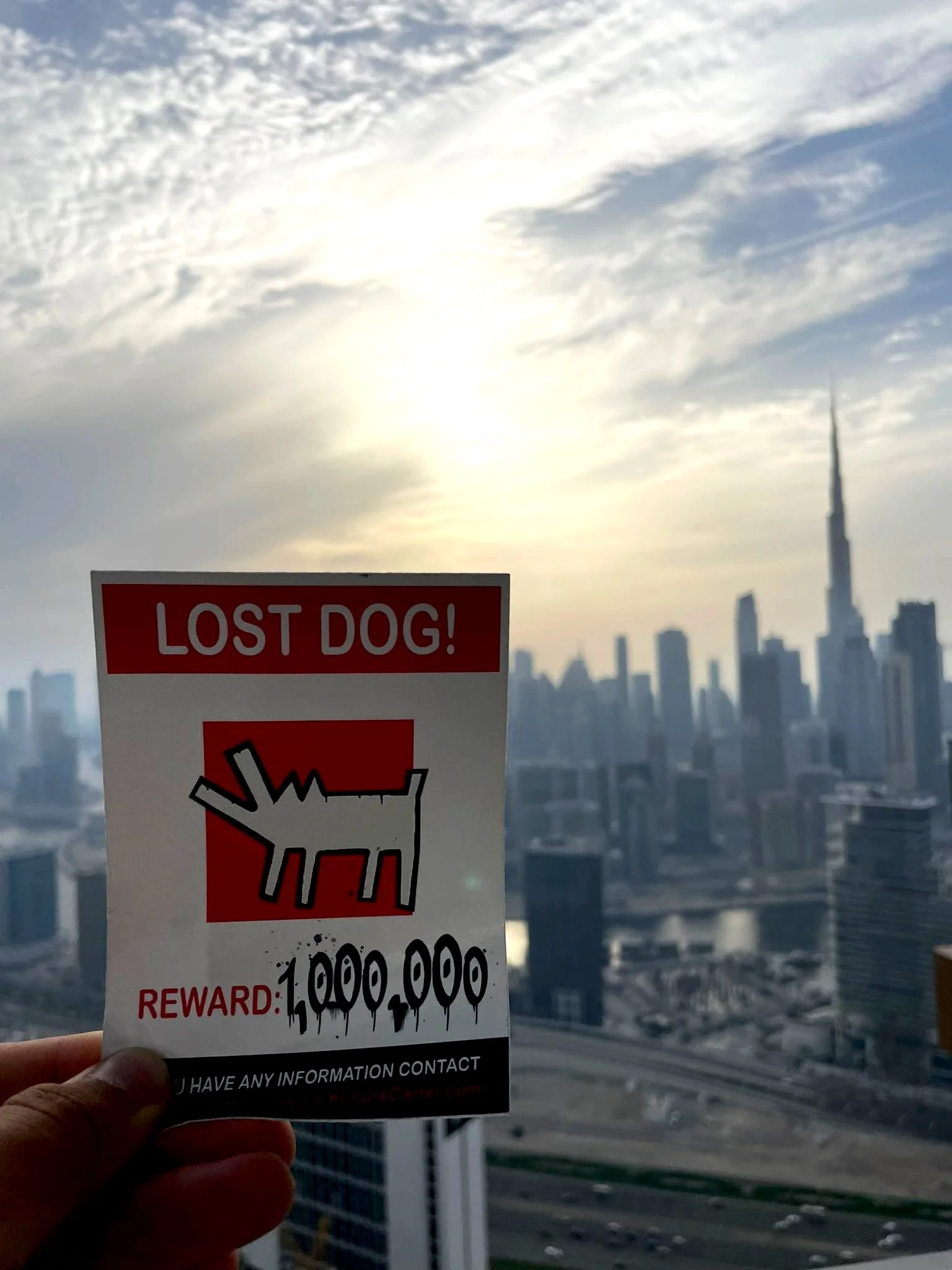 Lost dog sticker from Kulture Cartel being held in front of Dubai's landscape with Burj Khalifa silhouette as background