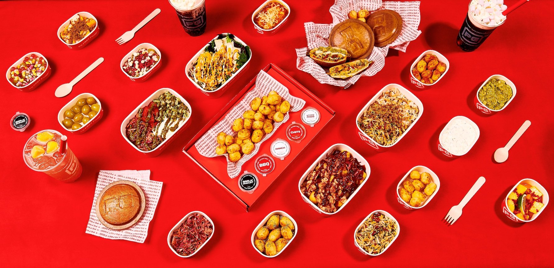 A spread of various dishes and drinks on a red table at Chick-fil-A, including salads, wraps, fried nuggets, sauces, apple slices, and two large milkshakes.
