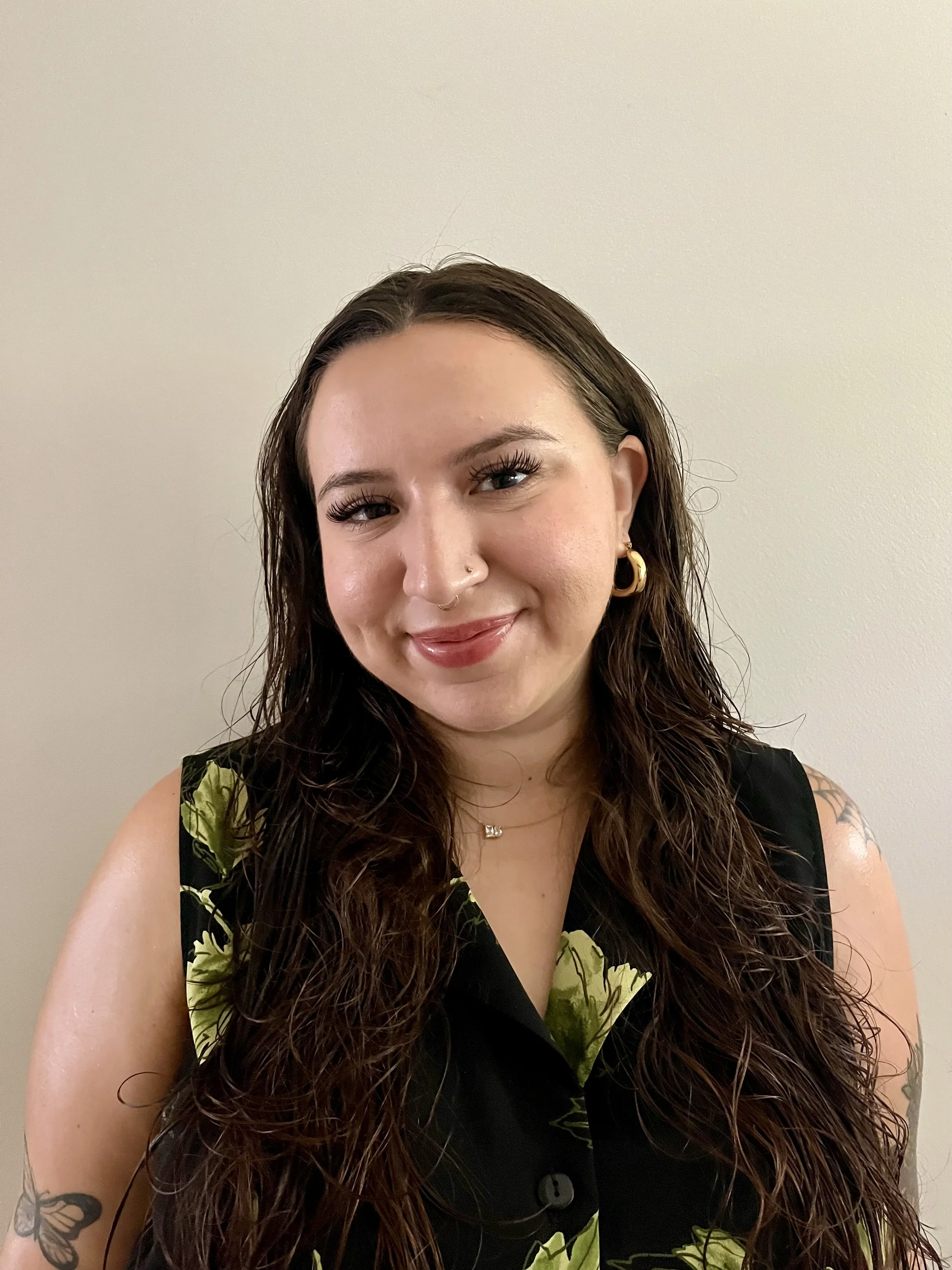 Photo of smiling woman with wavy brown hair and visible tattoos.