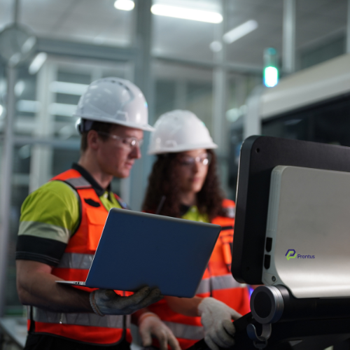 man and woman both wearing high visibility clothing and vests and looking at a laptop, discussin operational efficiency
