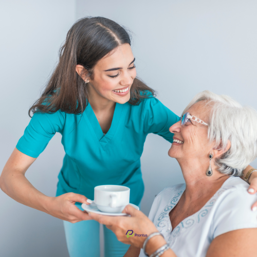 female care worker with brown hair and teal scrubs giving a cup of tea to an older lady with white hair and glasses, both are smiling
