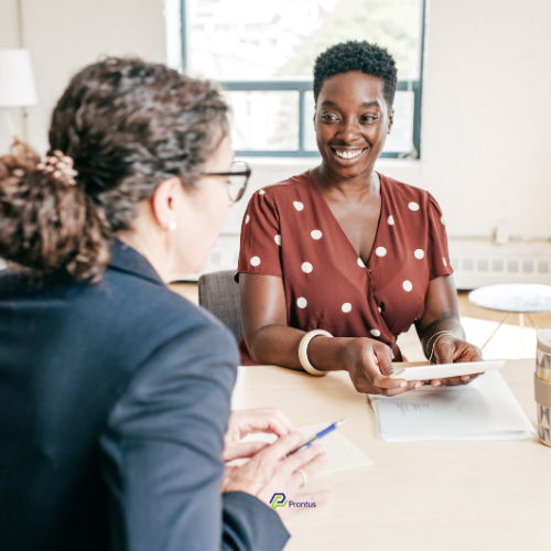 two women, one in a brown and white spot dress the other with brown hair in a navy jacket looking at financial paperwork as part of Making Tax Digital (MTD)