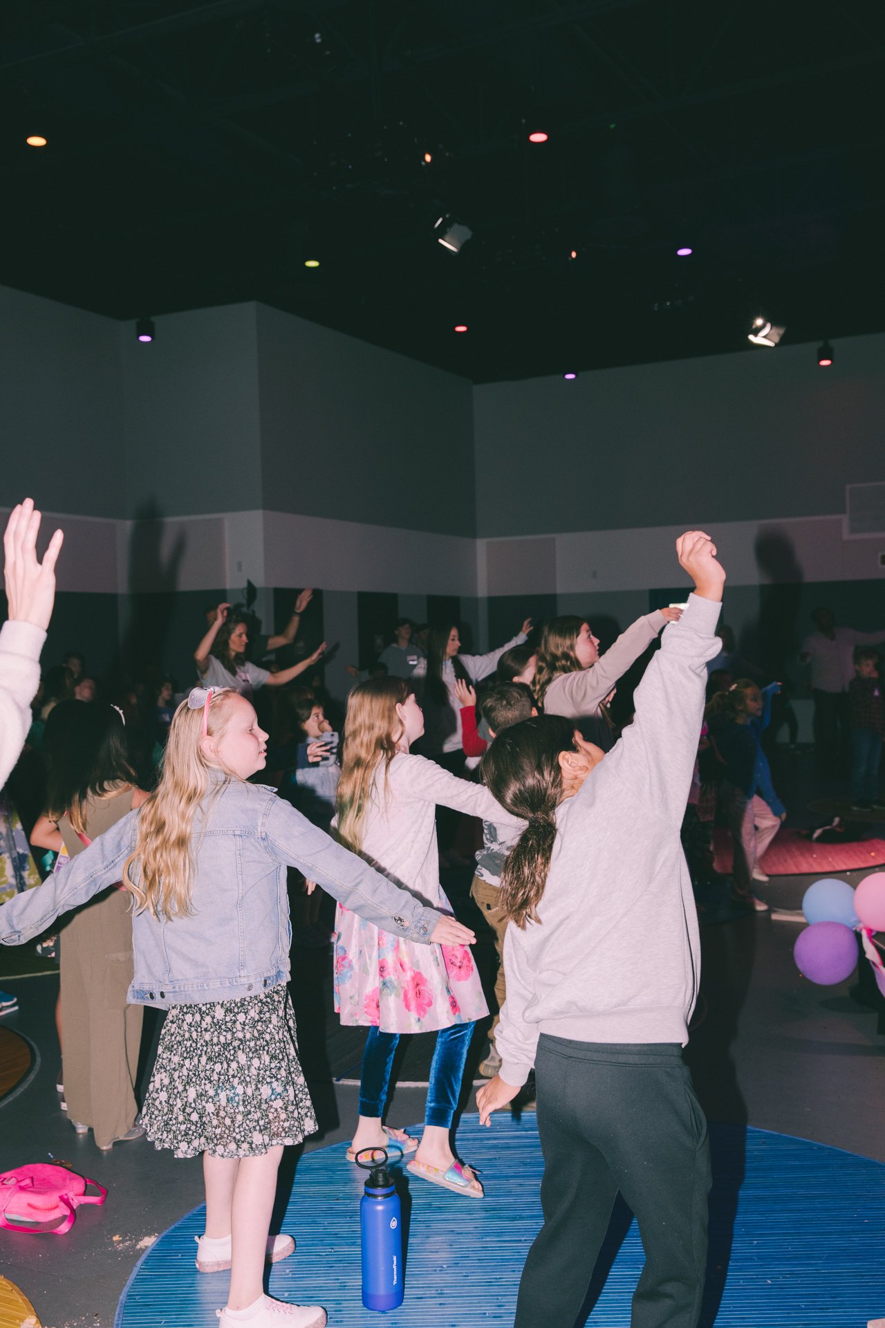 Children dancing at an indoor event with colorful lights.