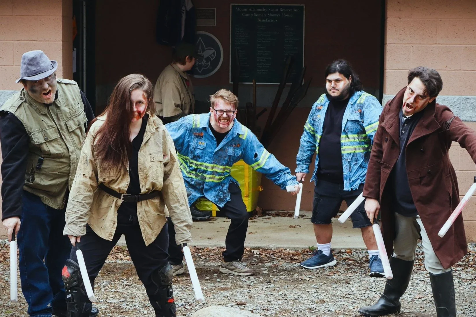 Six people dressed as zombies or monsters posing outside a building, with another person in the background near a sign.