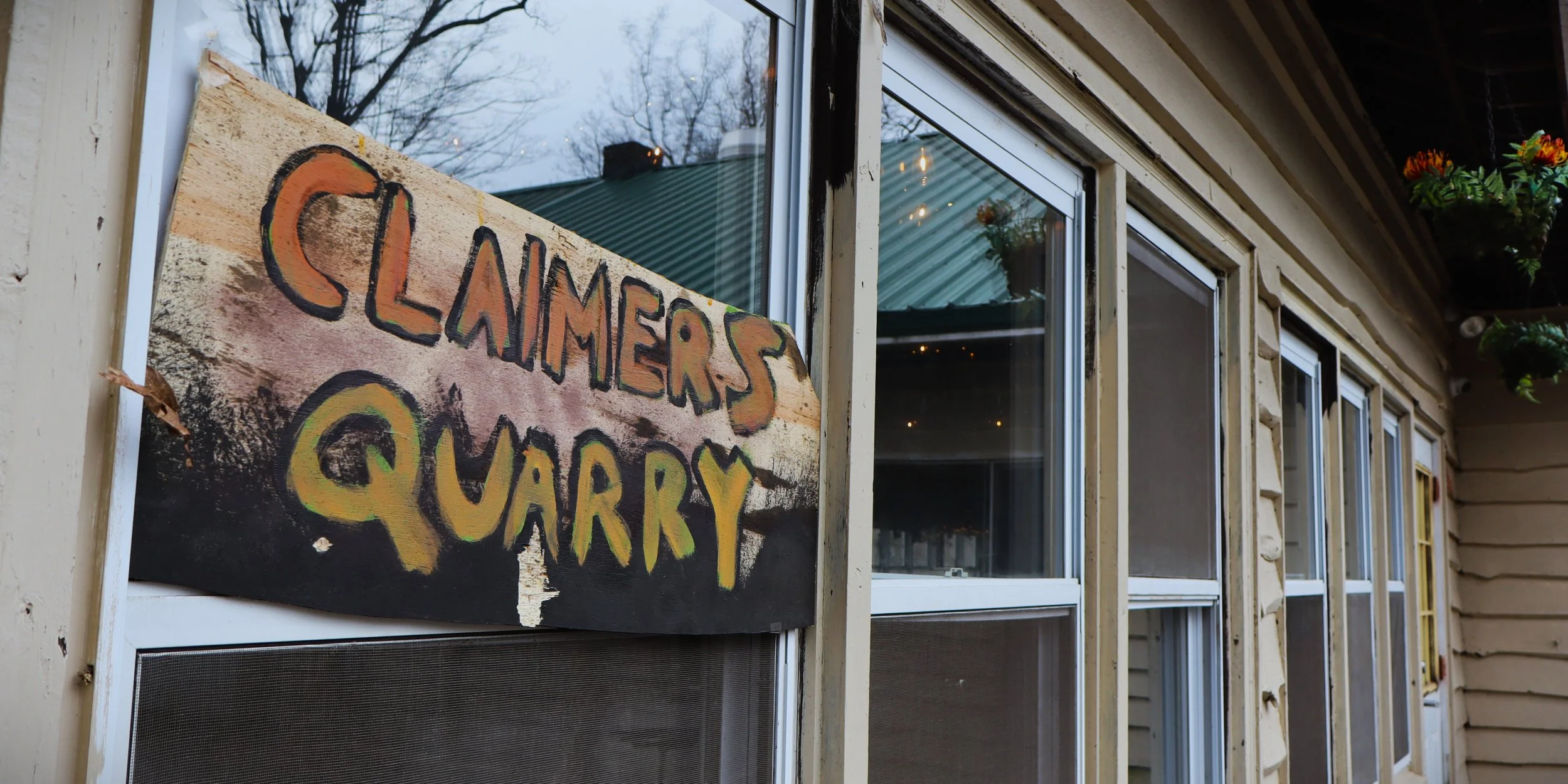 A wooden sign attached to a building window reads "Claimers quarry"..