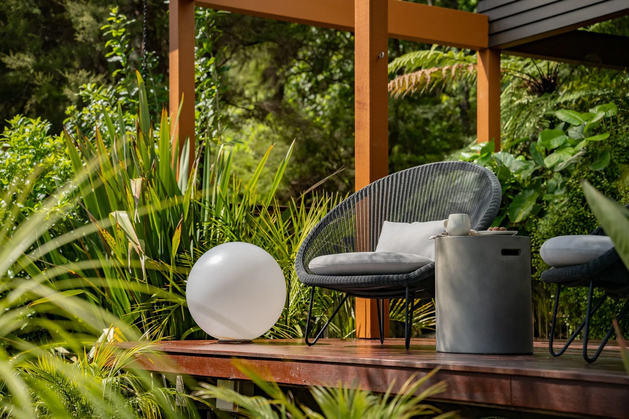 Outdoor patio with modern chairs, a white spherical lamp, and greenery.