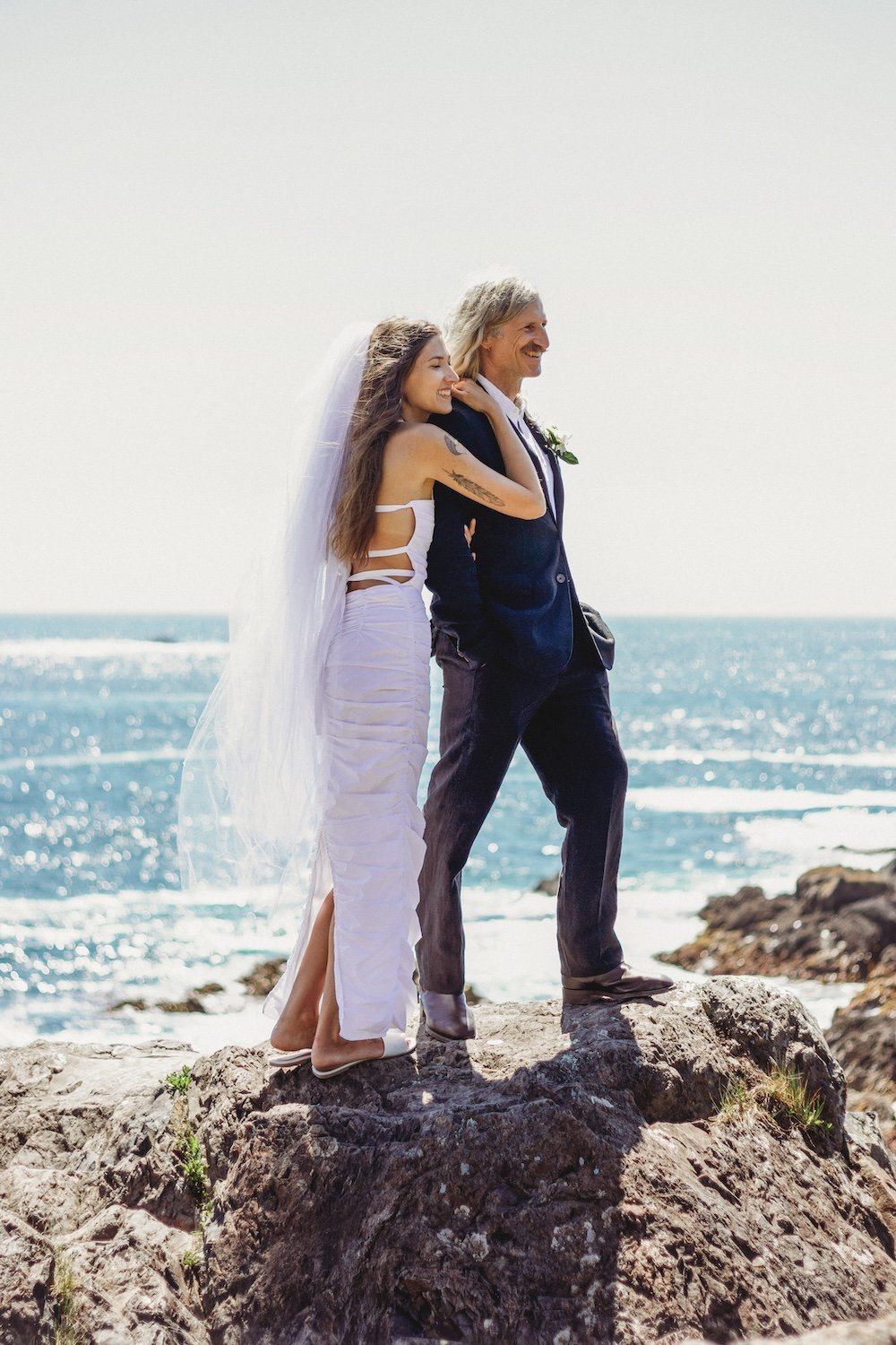 Bride and groom embracing on a rocky shoreline in Ucluelet