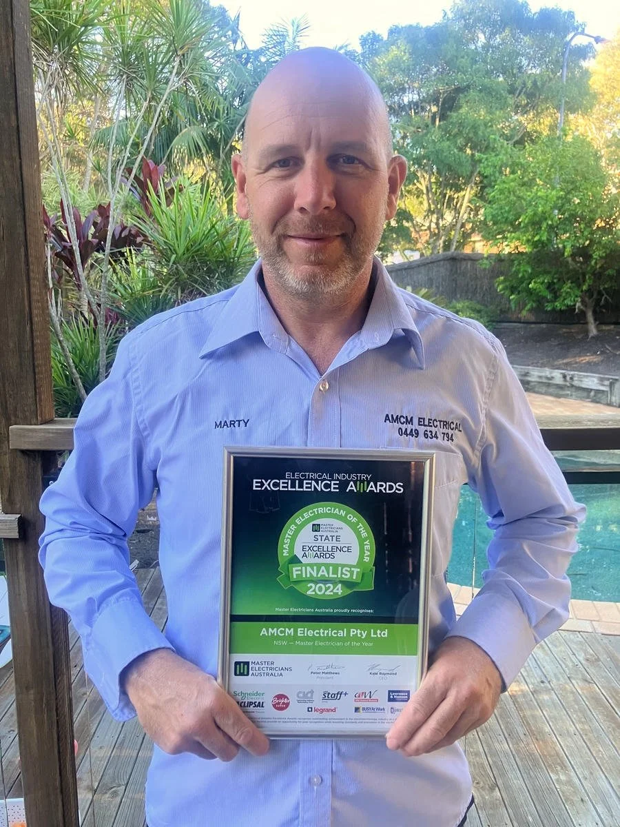 Marty Meehan wearing a light blue shirt holding a framed award certificate outside near a pool, with trees and plants in the background.