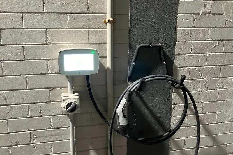 Electric vehicle charging station mounted on a brick wall with charging cable and plug.