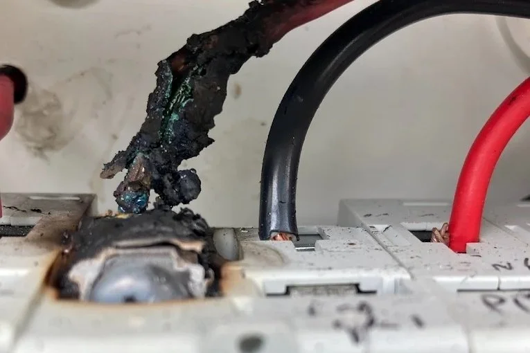 A close-up of a damaged electrical outlet with burnt and melted wires and connections.