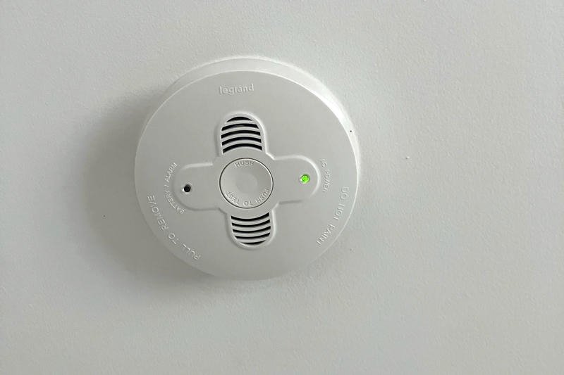 A smoke detector mounted on a white ceiling with a green indicator light.