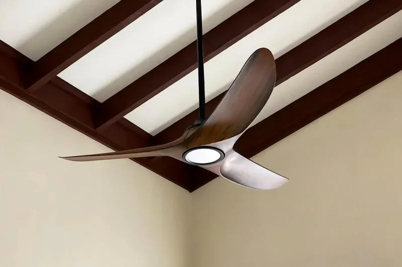 Modern ceiling fan with wooden blades and integrated light fixture, mounted on a ceiling with exposed wooden beams.