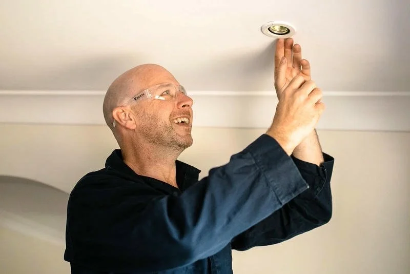 Electrician wearing protective glasses and a dark shirt, installing or adjusting a recessed ceiling light.
