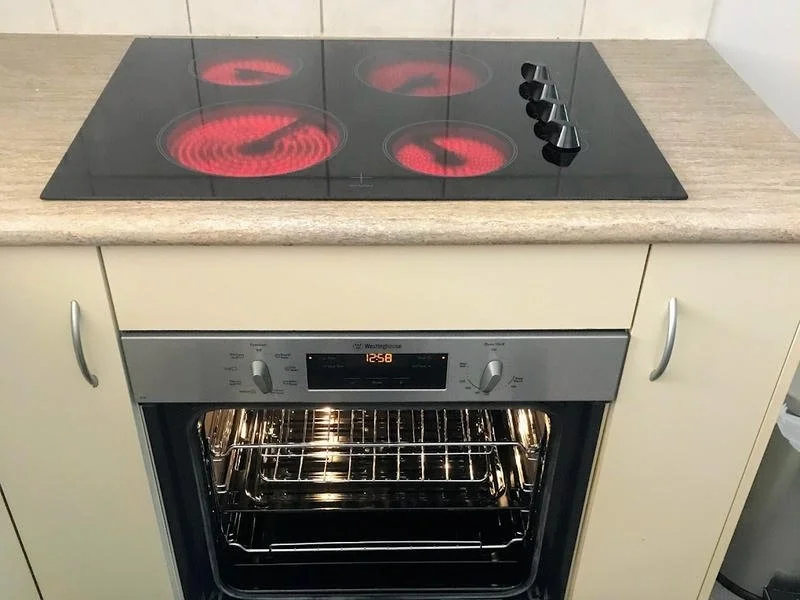 Electric stove with four burners, heating red hot, above an oven in a kitchen setting.
