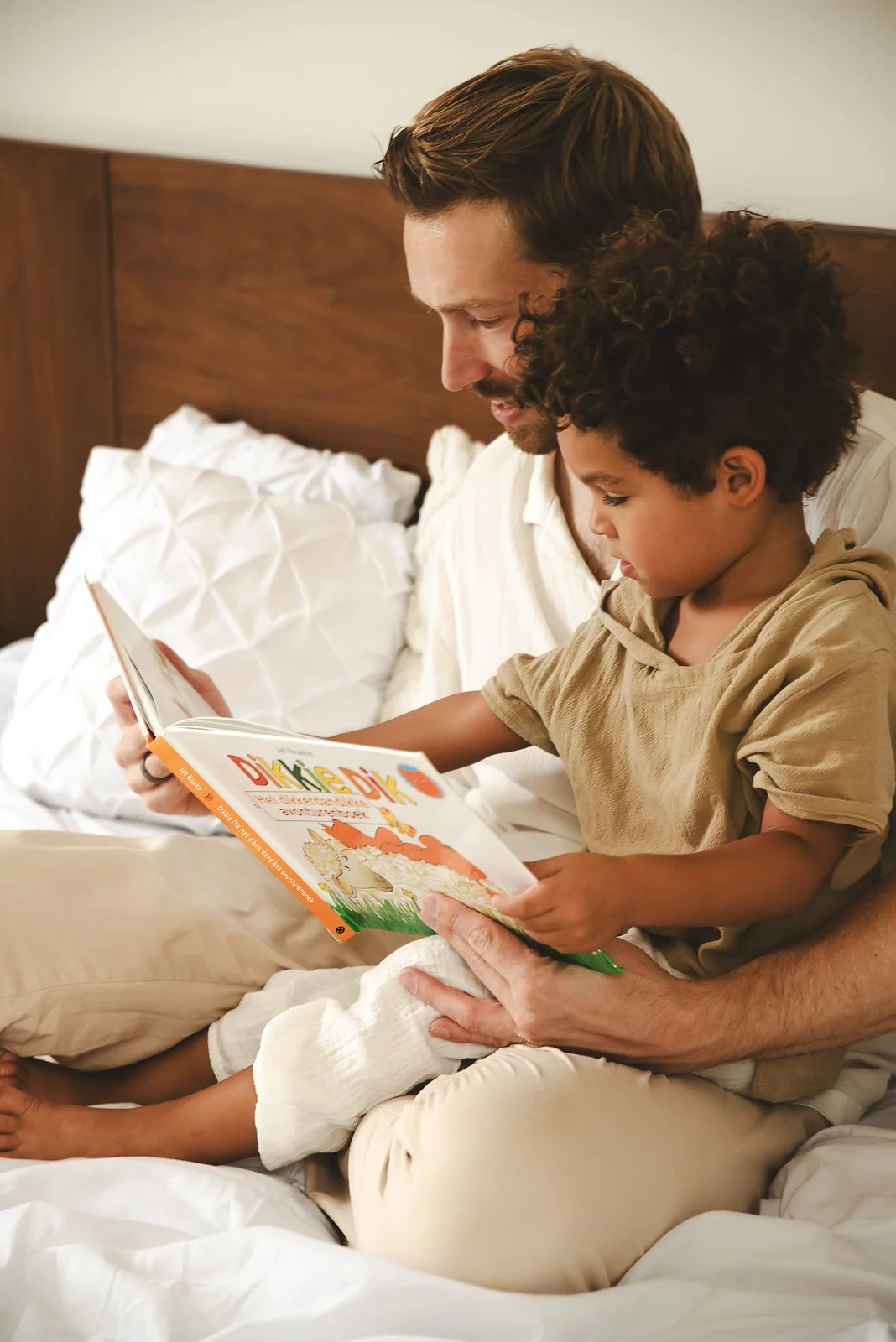A man and young boy sit together on a bed, reading a children's book in a family photoshoot in Tulum, Mexico.