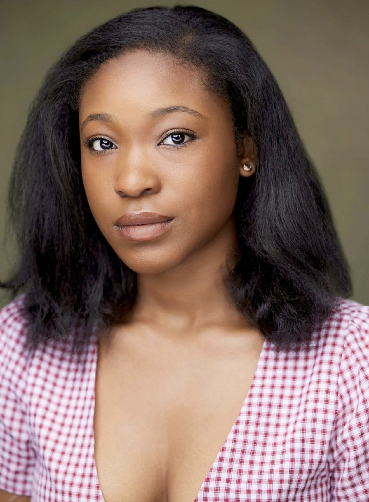 Headshot of Bianca Irene. Bianca is a medium brown/black African and American female between the ages of 16-27. She has straightened black hair for this photo and she is wearing a pink check top