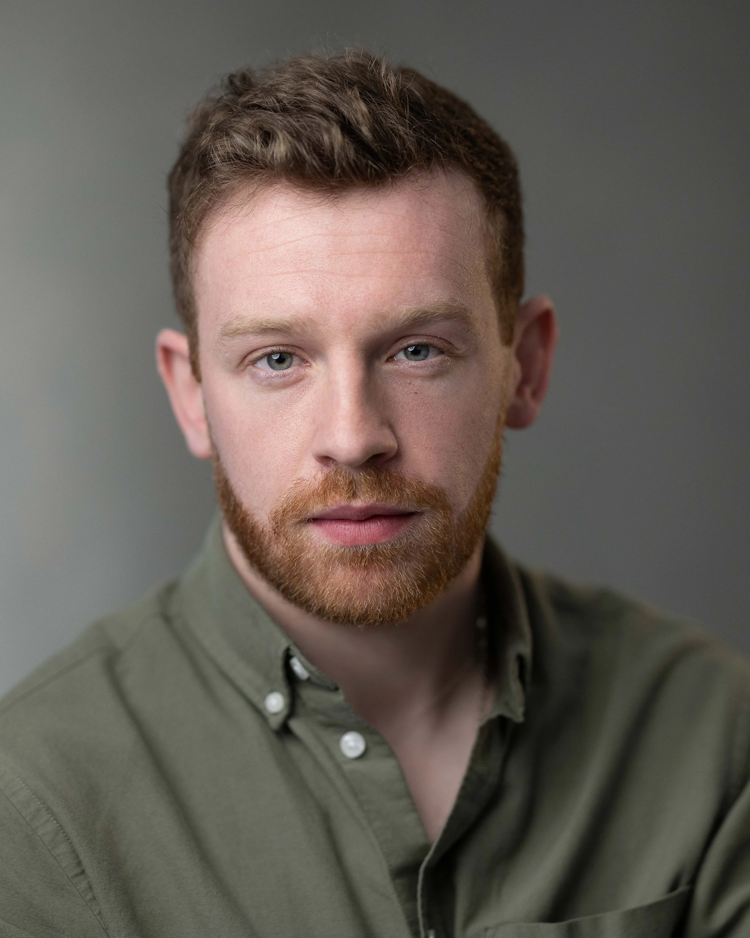 Headshot of actor Aaran Donoghue. Aaron is a caucasian male between the ages of 25-35. He has fair curly hair and is wearing a green shirt