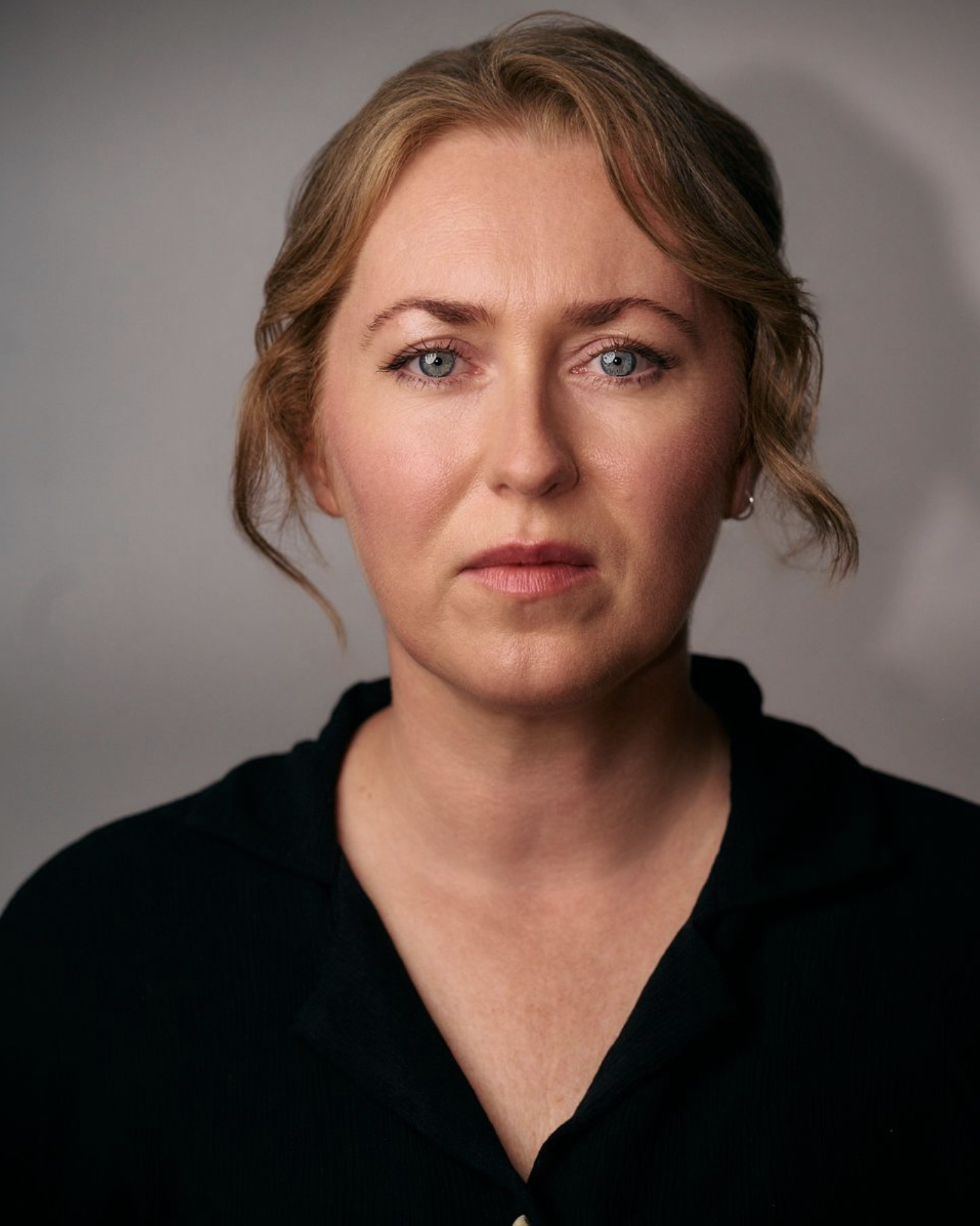 Headshot of Charlie Richardson. Charlie is an older female with ginger hair. She has white/freckled skin. She is wearing a black shirt and gold earrings.