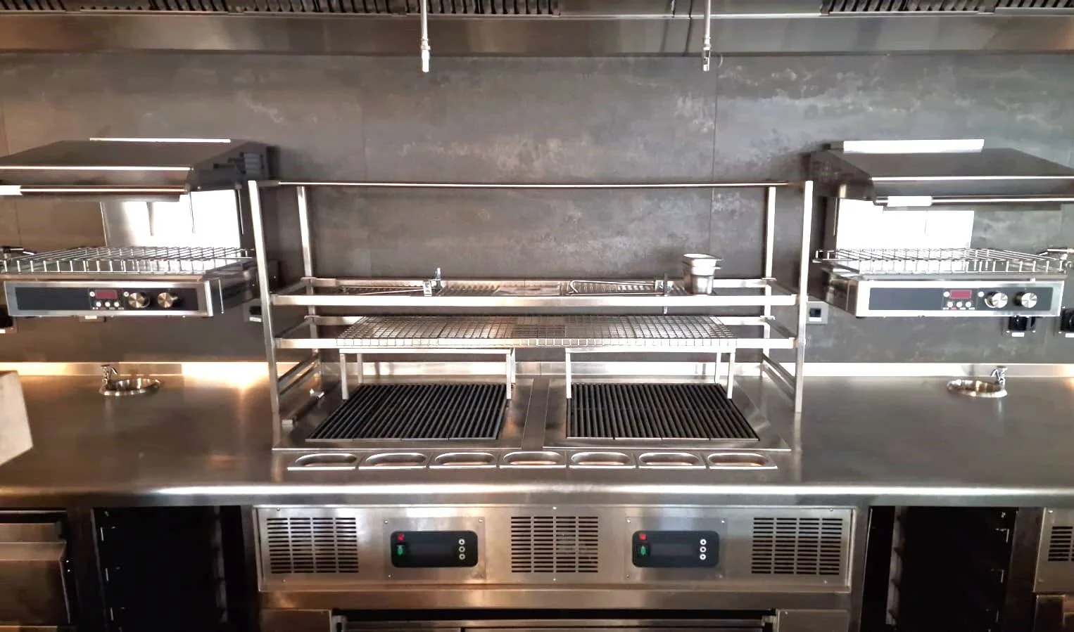 Industrial stainless steel kitchen with two deep fryers on either side, a central preparation table, and a gray wall in the background.