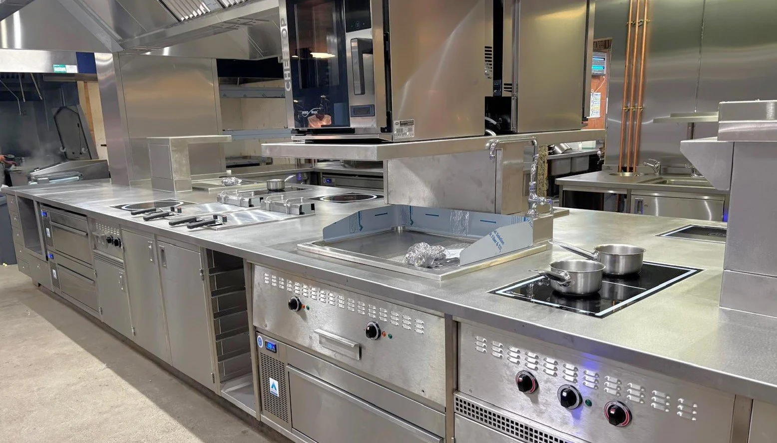 Commercial stainless steel kitchen with stovetop, oven, microwave, and various cookware