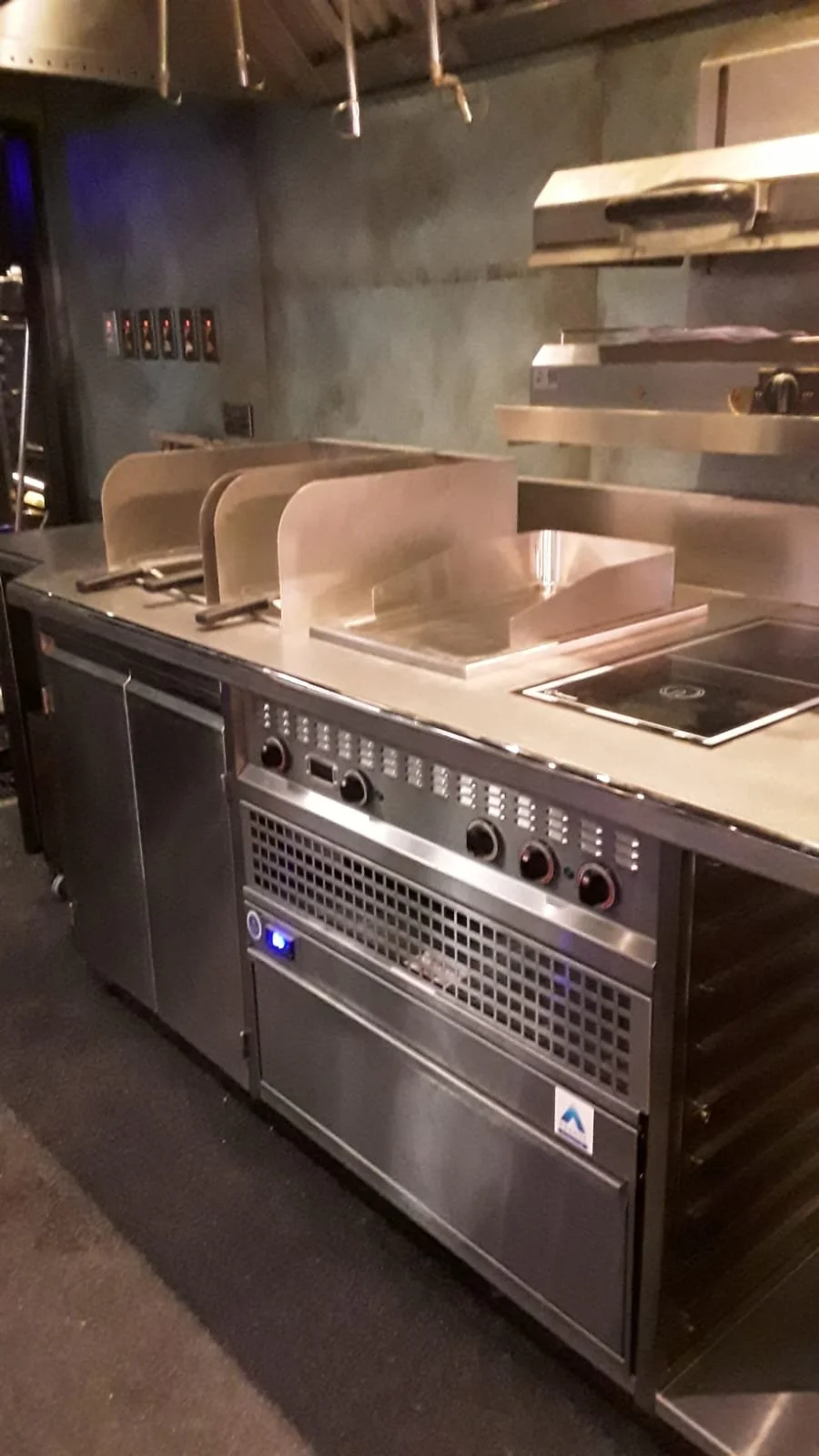 Commercial kitchen stove with metal dividers, control knobs, and a vent beneath, in a professional restaurant setting.