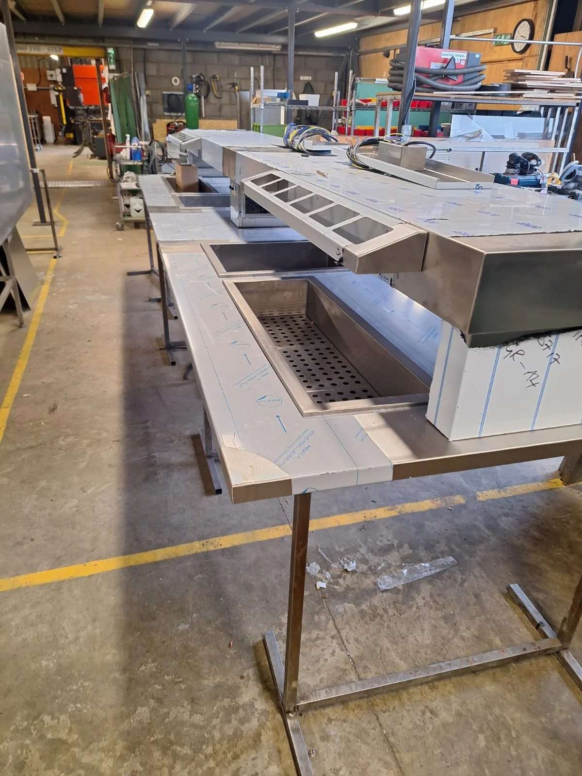 Metal work table with built-in sinks and ventilation hood in an industrial workshop.