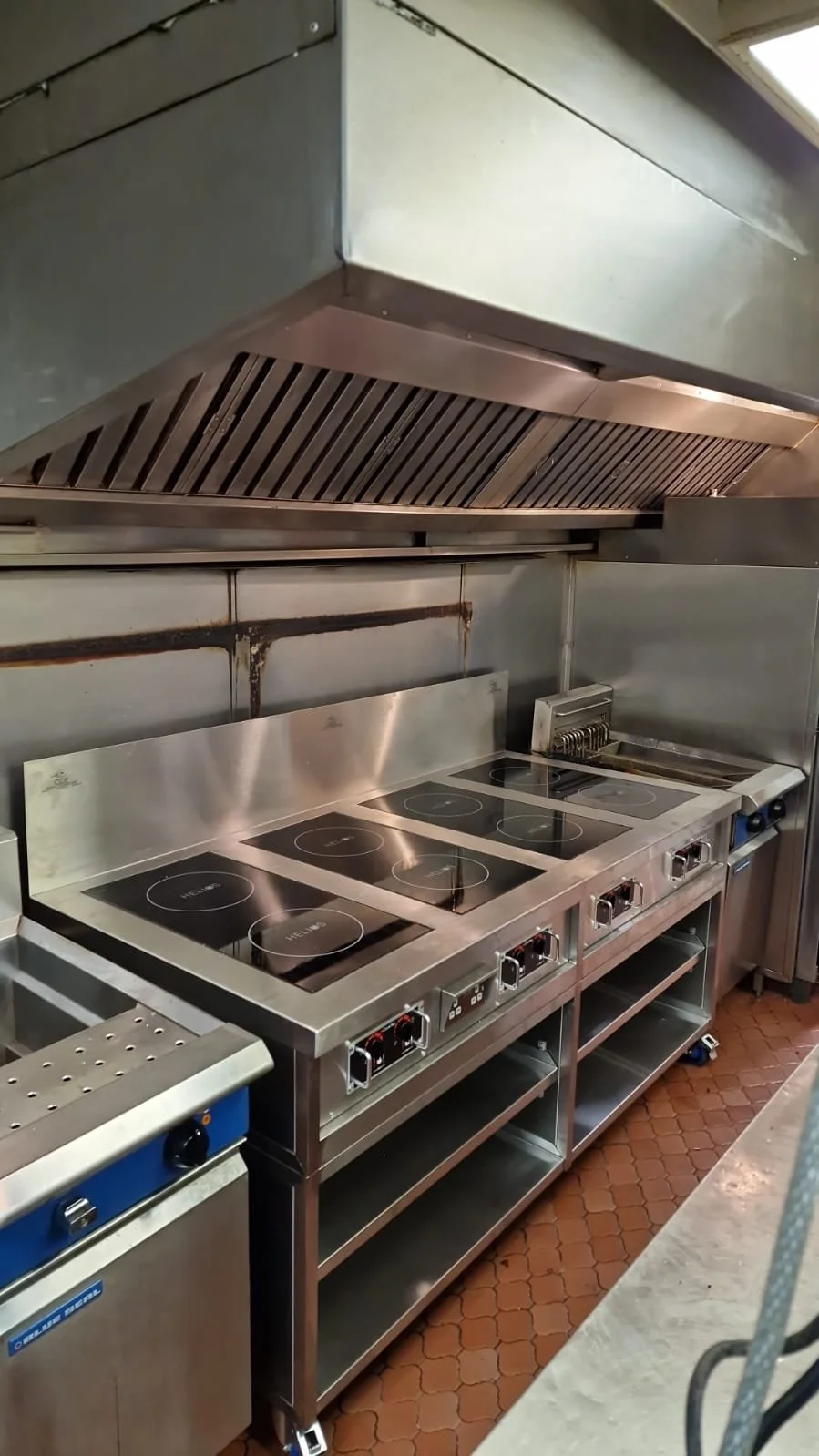 Commercial kitchen with stainless steel stove, grill, and oven under a stainless steel exhaust hood.