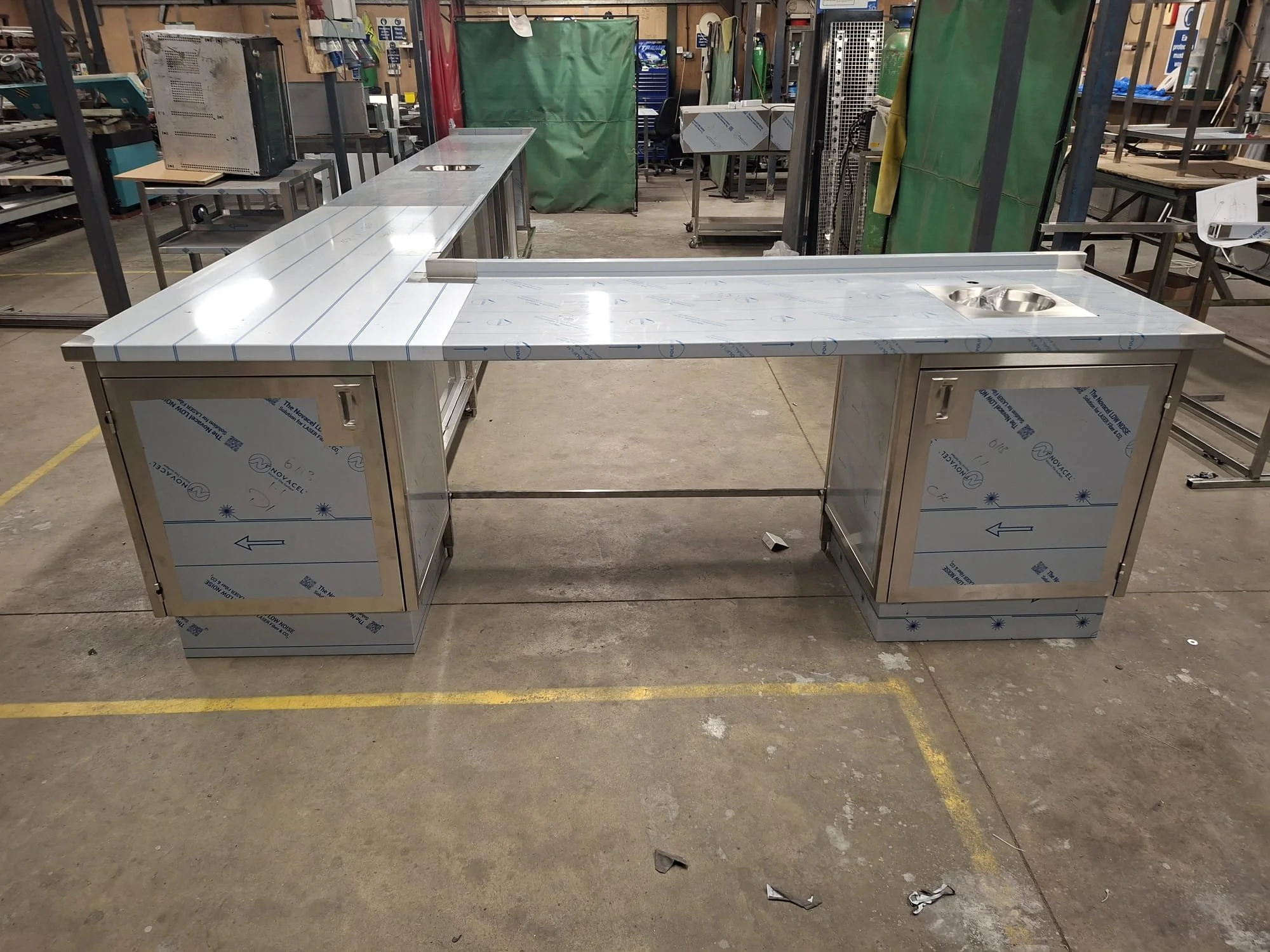 Stainless steel commercial kitchen counter with built-in sink, situated in an industrial workspace with tools and equipment in the background.