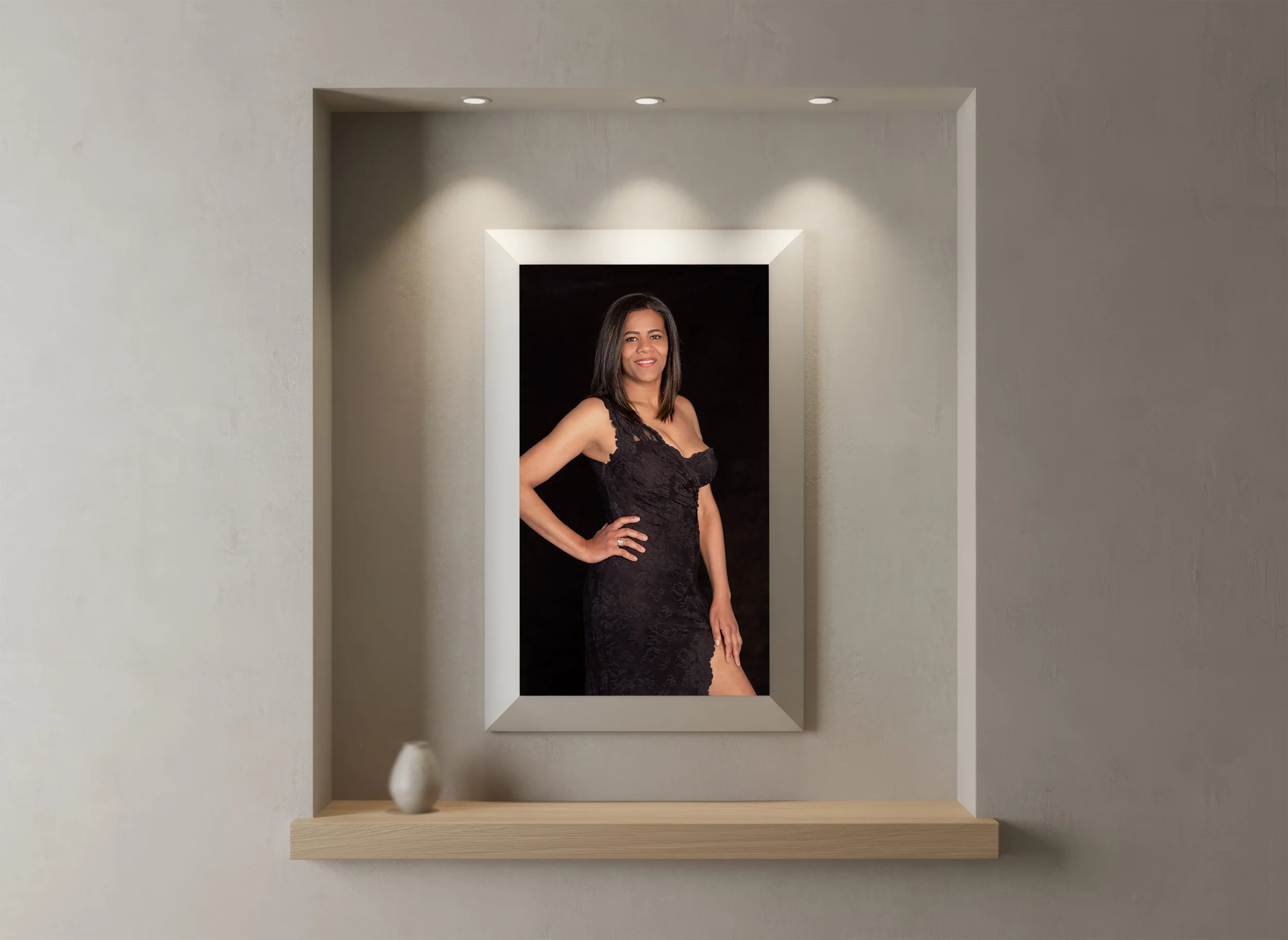A framed portrait of a woman in a black dress photographed by Monika M. Kubiak portrait photographer for women in Stuttgart., displayed on a wall with three overhead lights.