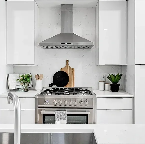Modern kitchen with white cabinets, stainless steel oven, black and wooden cutting boards, plants, and a range hood.