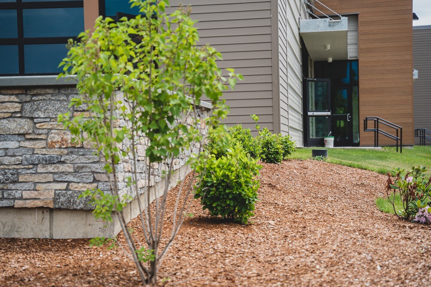 Admiring how the red mulch and shrubbery accentuates the beauty of the multi-colored brick and modern design at Williston's new Healthy Living. ⠀
⠀
An important example of how landscaping design is just as integral to your overall property look as bu
