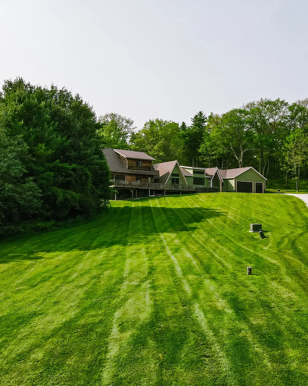 Wide view of a house with multiple levels and a large, well-manicured lawn surrounded by trees.