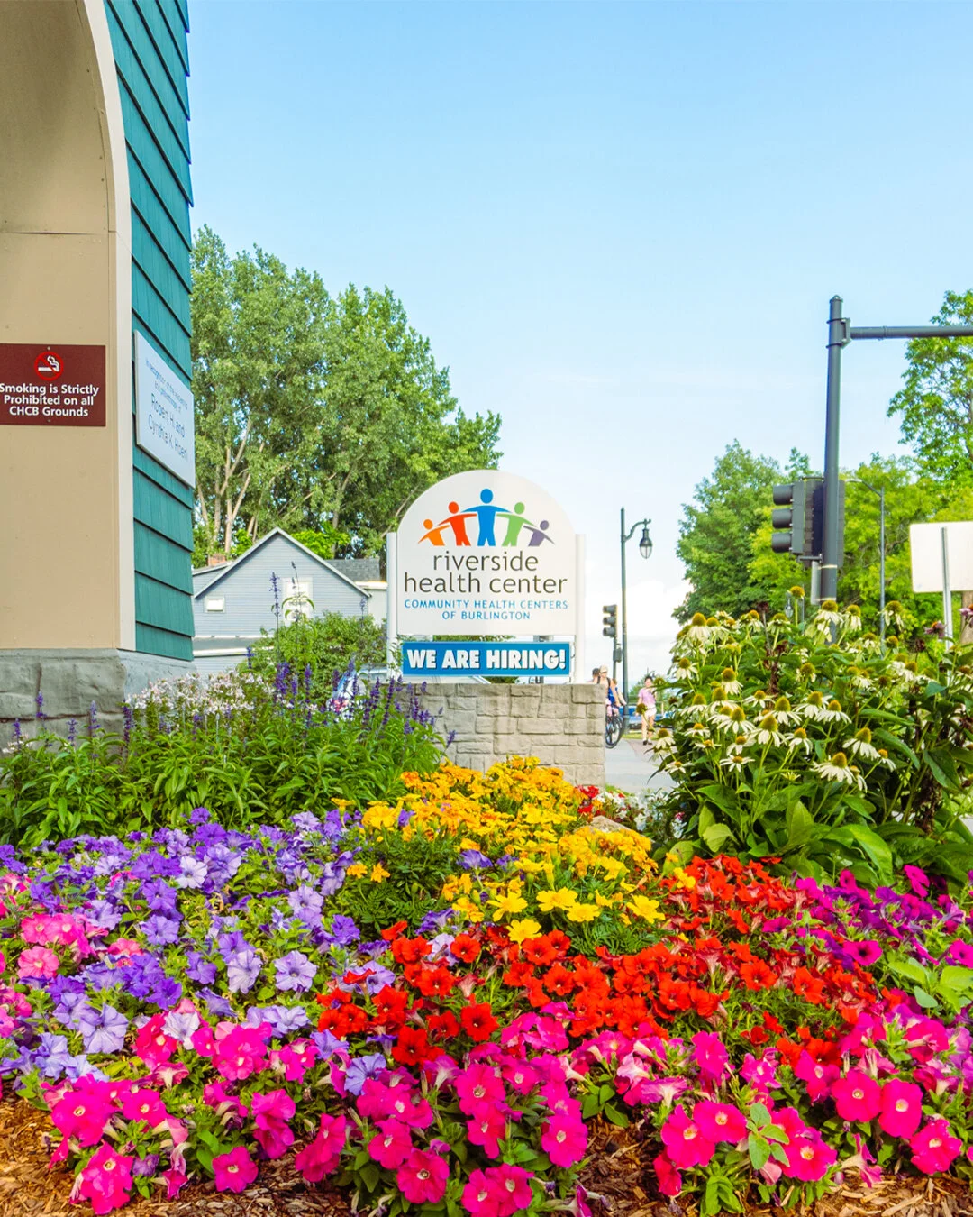Colorful flowers in front of Riverside Health Center sign with 'We Are Hiring!' notice.