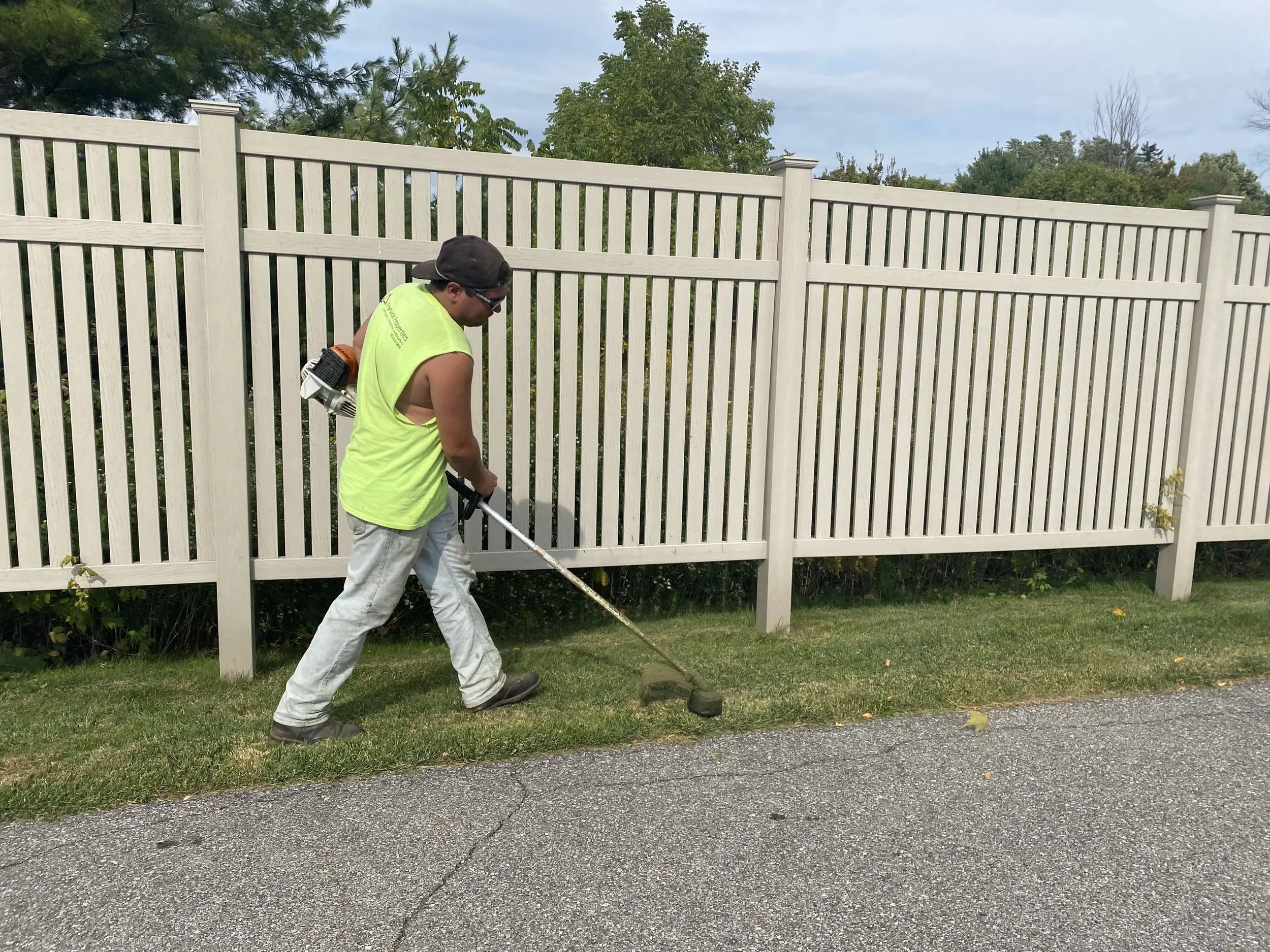 pinnacle properties worker weed whacking next to a fence