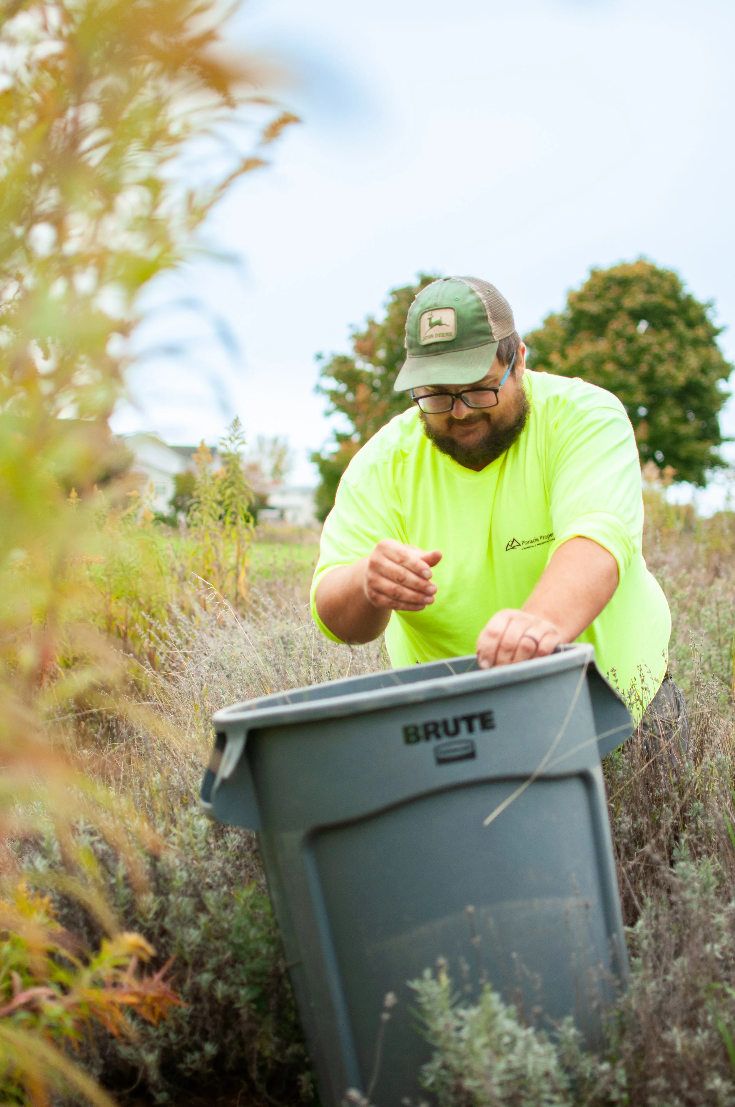 Man in neon yellow t-shirt places weeds in a trash bucket
