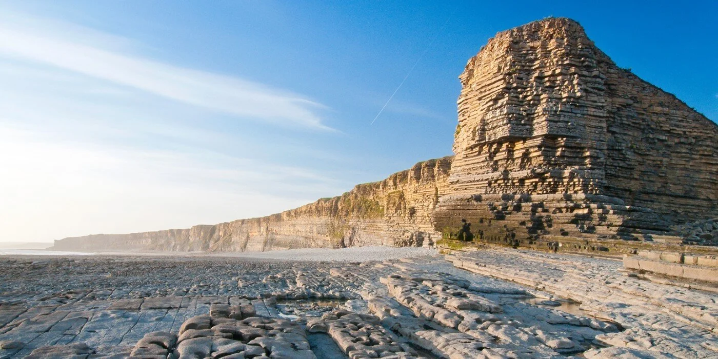 Cliffs along a rocky coastline under a clear sky with a faint contrail.