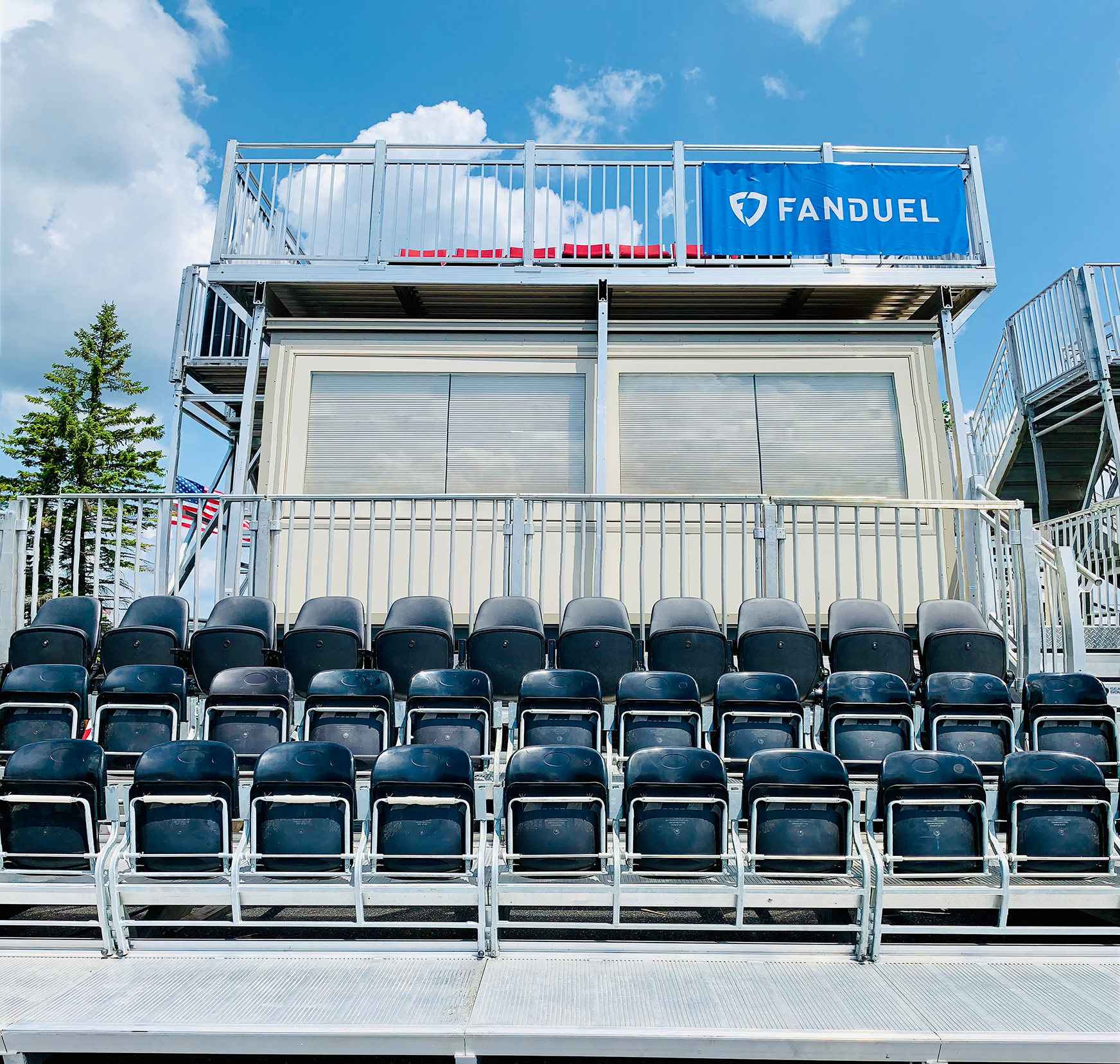 Empty bleacher seating at a sports stadium with a building and a FanDuel banner in the background.
