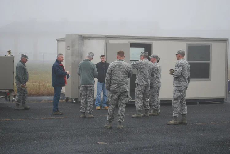 People in military uniforms standing beside a FORTS shelter