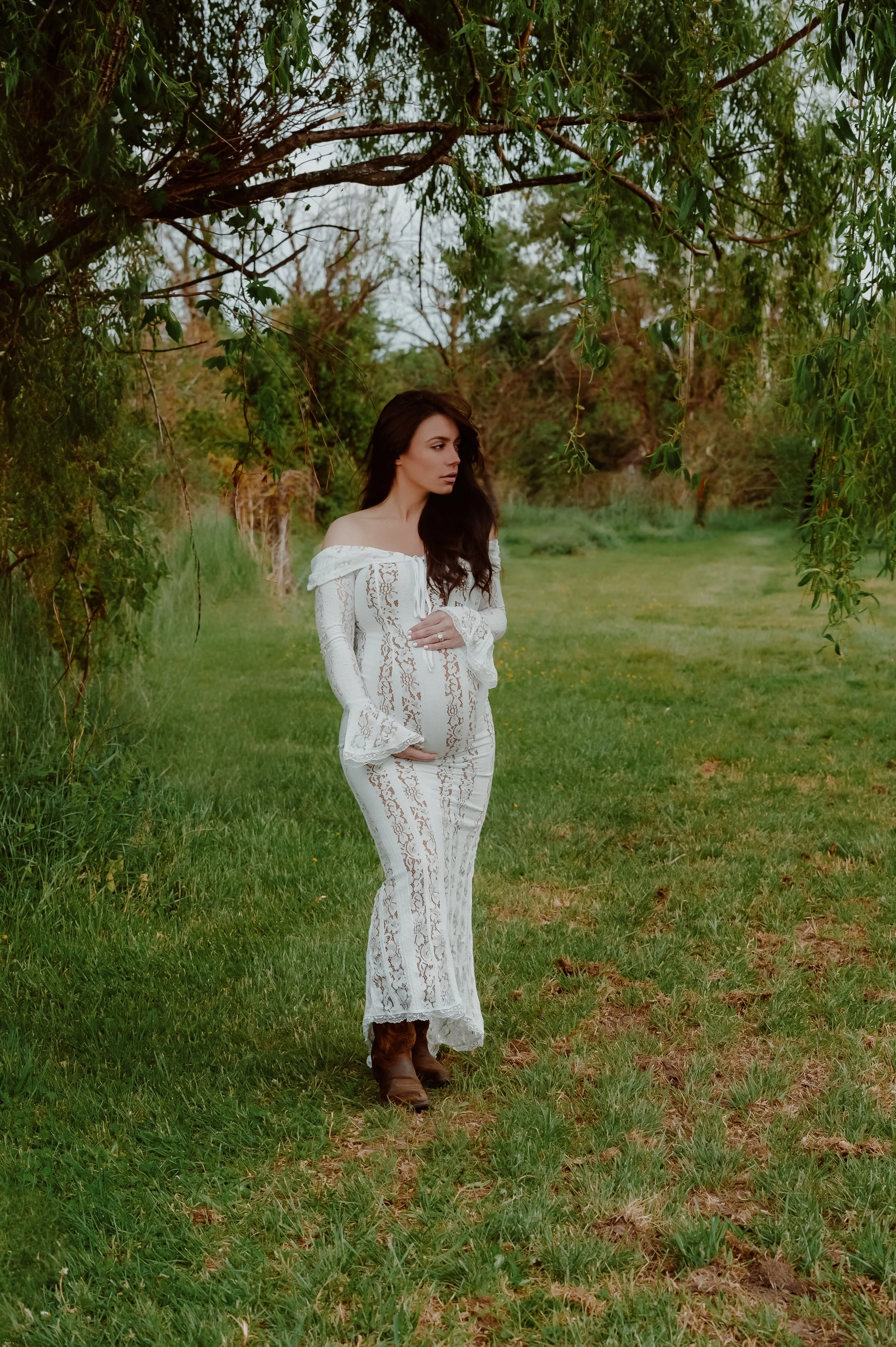 Outdoor portrait of an expecting mother wearing a white lace dress in a natural setting.