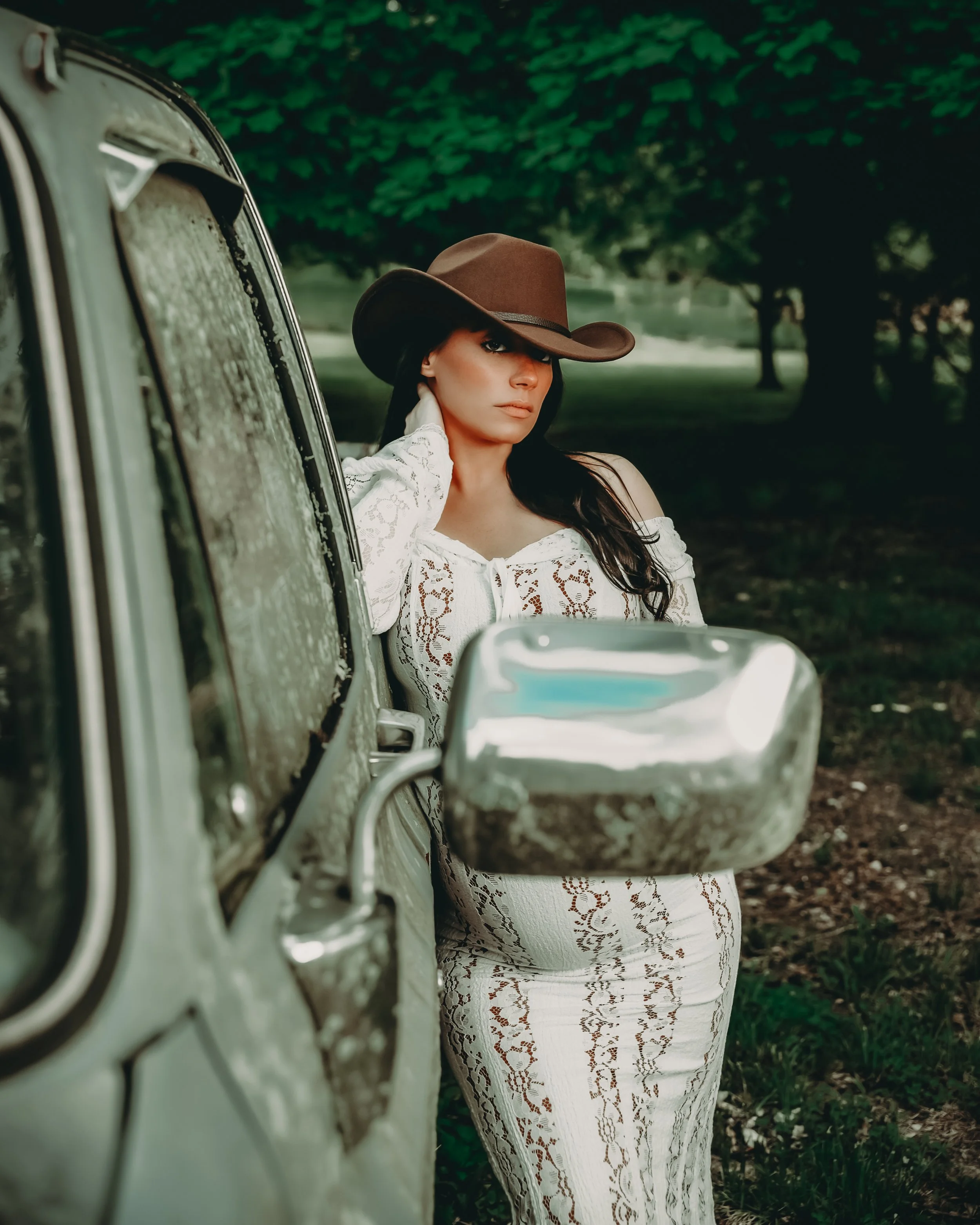 Country-inspired portrait of a woman wearing a cowboy hat beside a vintage truck.