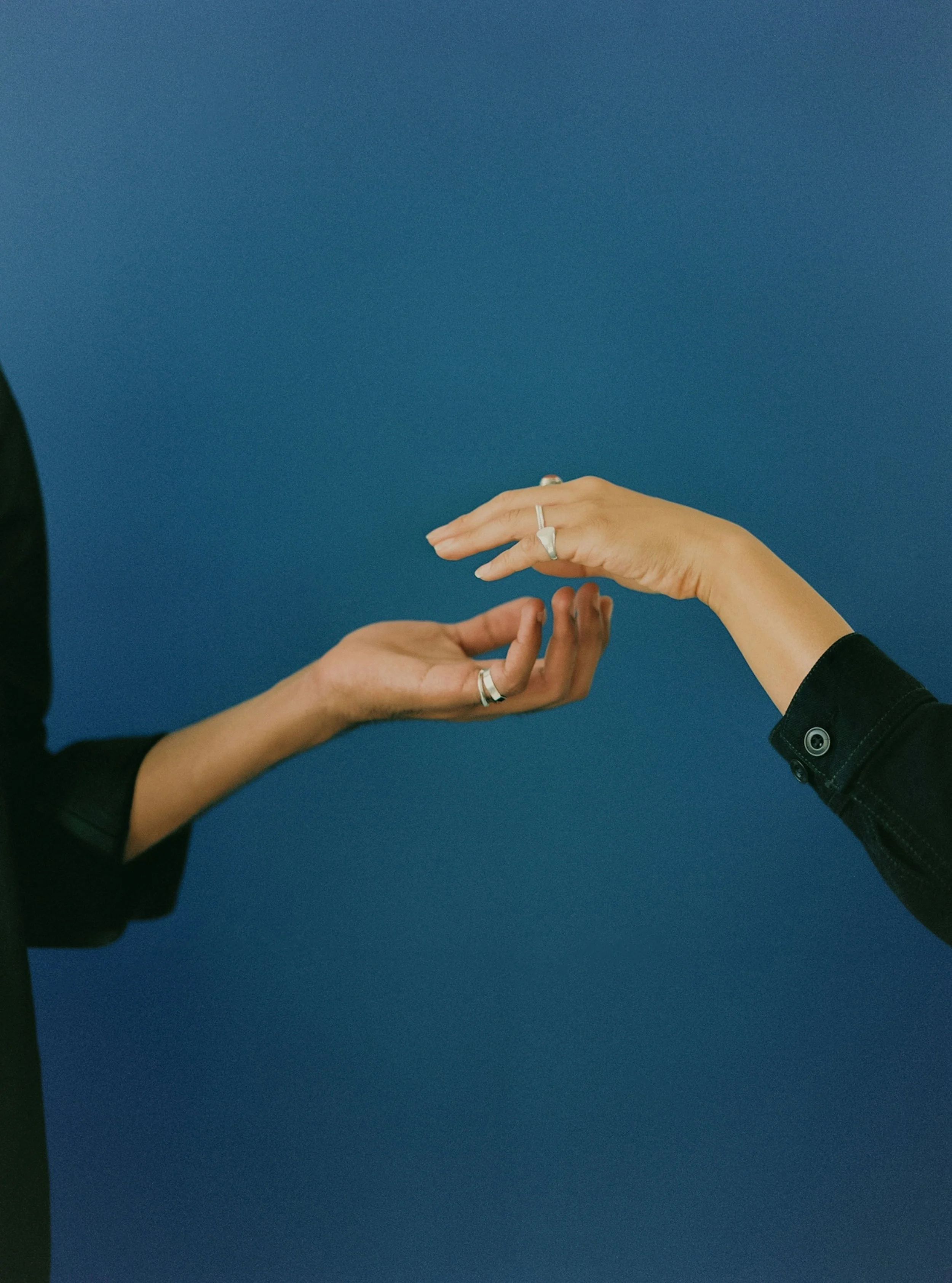 Two hands reaching out to each other against a blue background, with one hand slightly below the other and gesturing as if to touch.